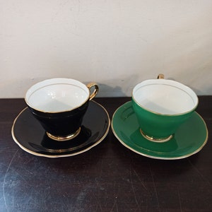 May include: Two teacups and saucers, one black with gold trim and one green with gold trim.