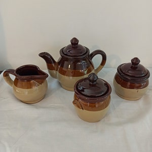 May include: A set of four brown and beige ceramic tea and sugar containers. The set includes a teapot, a creamer, a sugar bowl, and a lidded sugar bowl.