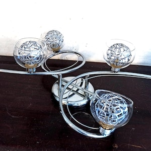 Peut inclure: Un lustre moderne en chrome avec six globes en verre transparent. Chaque globe contient une sphère en fil d'argent. Le luminaire est posé sur une surface marron foncé. Design épuré et contemporain, idéal pour divers intérieurs.