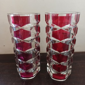 May include: Two clear glass vases with a geometric pattern and a deep red color. The vases are tall and slender, with a hexagonal base.