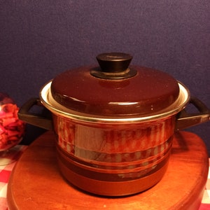 May include: A brown and red enamel pot with a black lid and handle. The pot has a striped pattern and a gold rim.