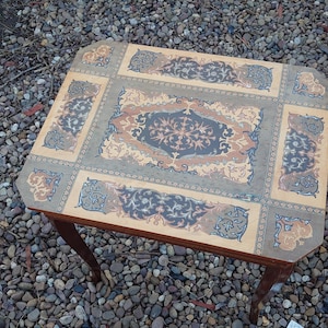 May include: A wooden table with intricate inlaid designs in shades of brown, blue, and gold. The table has a square top and four legs.