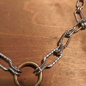 May include: A silver chain necklace with a large, round, brass ring pendant.