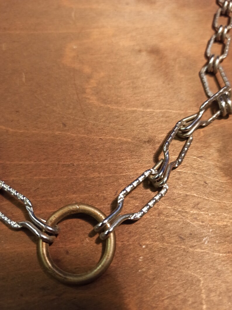 May include: A silver chain necklace with a large, round, brass ring pendant.