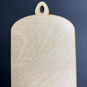 May include: A light-colored, unfinished wooden plaque with a rounded top and a small hole for hanging. The plaque has a smooth surface and a natural wood grain pattern. The shape is rectangular with rounded edges.