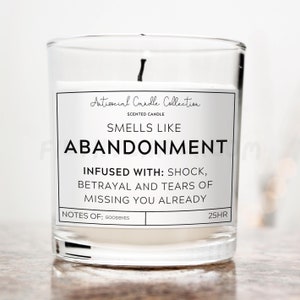 以下が含まれることがあります： 透明なガラスの香りのキャンドル。白いラベルには「Antisocial Candle Collection」と「Smells Like Abandonment」と書かれています。成分が記載されており、燃焼時間は25時間です。