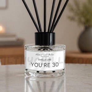 Puede incluir: Un difusor de varillas de vidrio transparente con tapa negra y seis varillas negras. La etiqueta rectangular blanca presenta el texto "Antisocial Scent Collection" y "SMELLS LIKE YOU'RE 30" en letras negras, con un borde negro fino.