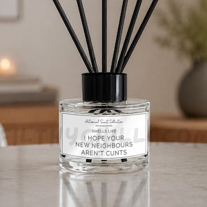 Op de afbeelding: Een doorzichtige glazen diffuserfles met een zwarte dop en zes zwarte rietjes. Het witte rechthoekige etiket bevat de tekst: Antisocial Scent Collection, SMELLS LIKE I HOPE YOUR NEW NEIGHBOURS AREN'T CUNTS, gedrukt in een zwart schreefloos lettertype.