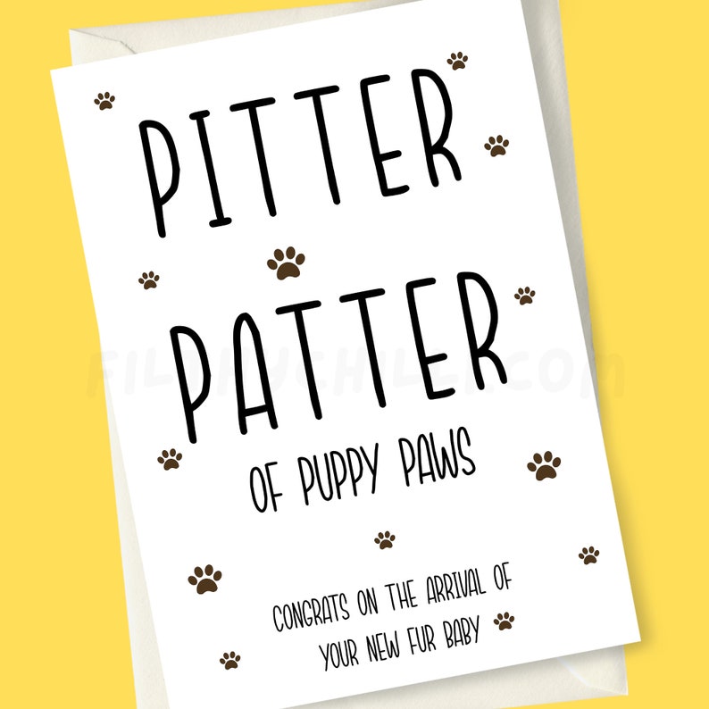 May include: A white card with black text that reads "Pitter Patter of Puppy Paws" and "Congrats on the arrival of your new fur baby". The card is decorated with brown paw prints.