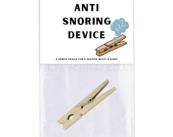 Könnte beinhalten: Eine weiße Verpackung mit einer kleinen Holz-Wäscheklammer im Inneren. Auf der Verpackung steht "ANTI SNORING DEVICE" und "A HANDY DEVICE FOR A RESTFUL NIGHT'S SLEEP".