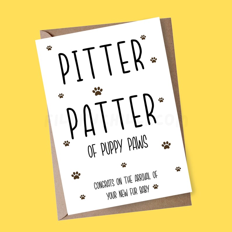 May include: A white card with black text that reads "Pitter Patter of Puppy Paws" and "Congrats on the arrival of your new fur baby". The card is decorated with small paw prints.