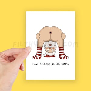 May include: A white Christmas card featuring a cartoon Santa Claus bent over, with his backside visible. Santa's legs are in red and white striped socks. The text "HAVE A CRACKING CHRISTMAS" is printed below the illustration.
