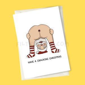 May include: A white Christmas card featuring a cartoon Santa Claus bent over, with his backside on display. Santa's legs are seen, wearing red and white striped socks. The card reads "HAVE A CRACKING CHRISTMAS" in black text.