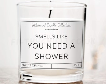 Op de afbeelding: Een glazen kaars pot met een wit label waarop staat "Antisocial Candle Collection" en "Smells Like You Need A Shower". Het label bevat ook "Notes of: Vanilla" en "25HR".