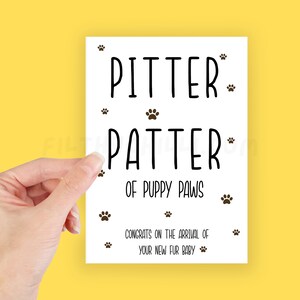 May include: White card with black text that reads "Pitter Patter of Puppy Paws" and "Congrats on the arrival of your new fur baby". The card is decorated with small paw prints.