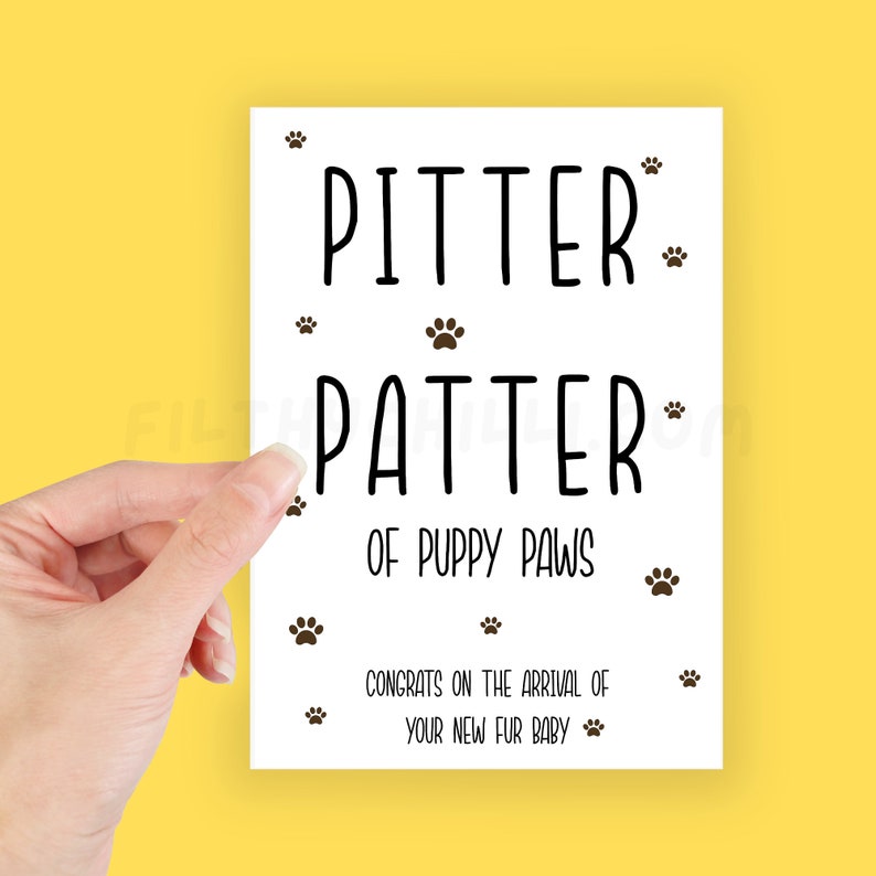 May include: White card with black text that reads "Pitter Patter of Puppy Paws" and "Congrats on the arrival of your new fur baby". The card is decorated with small paw prints.