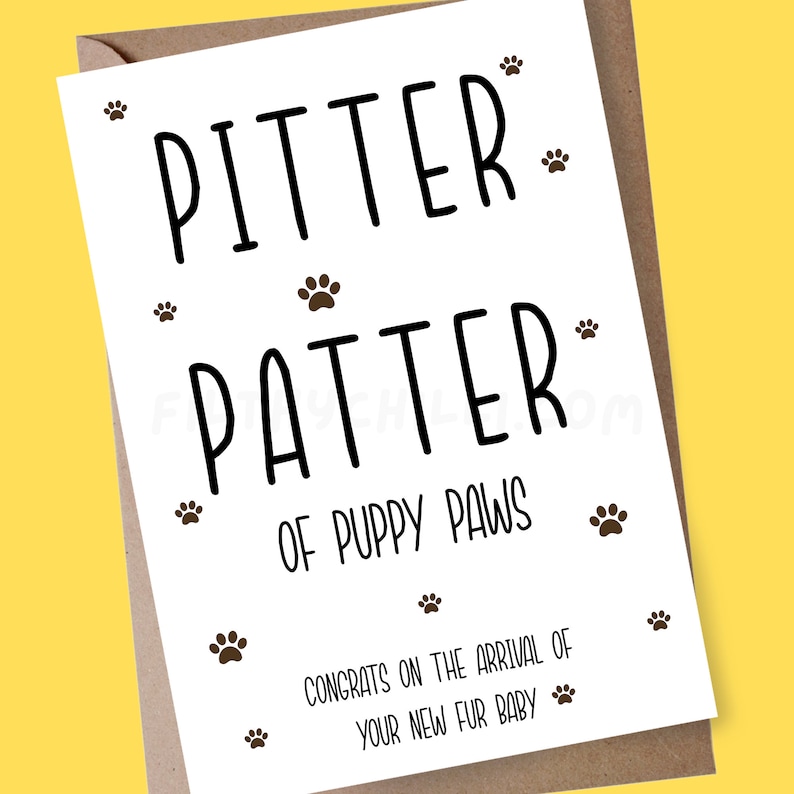 May include: A white card with black text that reads "Pitter Patter of Puppy Paws" with brown paw prints scattered around the text. The bottom of the card reads "Congrats on the arrival of your new fur baby."