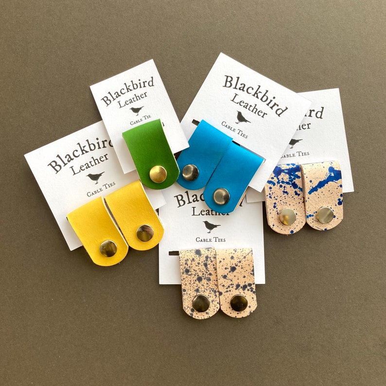 May include: Four pairs of leather cable ties in different colours and patterns. The ties are made by Blackbird Leather and are labelled "Cable Ties".