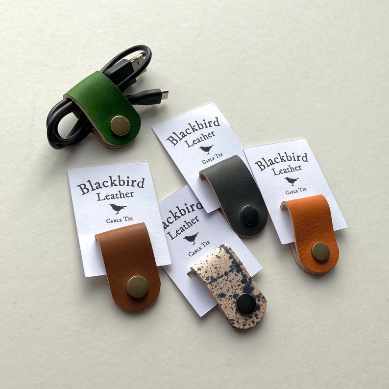 May include: Five leather cable ties in different colours and patterns. The ties are labelled "Blackbird Leather" and "Cable Tie".