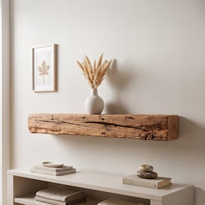 Könnte beinhalten: Ein rechteckiges Wandregal aus natürlichem, verwittertem braunem Holz mit rauer, strukturierter Maserung. Das Regal ist horizontal montiert und trägt eine weiße Keramikvase, die mit getrockneten beigen Pampasgrasstängeln gefüllt ist.