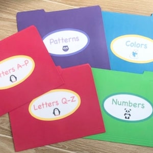 May include: A collection of colorful file folders labeled with educational themes. The folders are red, purple, blue, and green, each with a white oval sticker. The stickers display words like "Letters A-P," "Patterns," and "Colors," with accompanying illustrations.