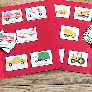 May include: A red folder with two flaps, divided into sections, each with a picture of a different vehicle, such as a school bus, fire truck, ambulance, tow truck, mail truck, tractor, taxi, garbage truck, police car, airplane, cement mixer, bulldozer, crane, and excavator. The words below each picture identify the vehicle.
