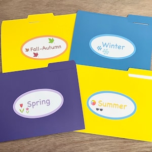 May include: Four yellow, blue, purple, and yellow file folders with labels for each season. The labels are oval-shaped with a white background and black text. The labels read "Fall-Autumn", "Winter", "Spring", and "Summer". Each label has a small graphic representing the season.