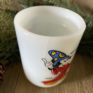 May include: White ceramic mug with a cartoon image of Mickey Mouse as a sorcerer. Mickey is wearing a blue hat with stars and a red robe. The mug has the text "Mickey Mouse" and "1940" printed on it.