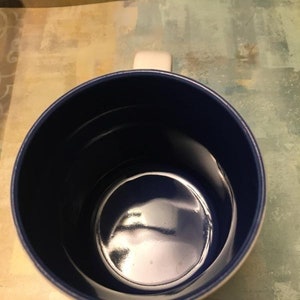 Puede incluir: Una taza de cer&aacute;mica blanca con interior azul. La taza tiene un asa en el lado derecho.