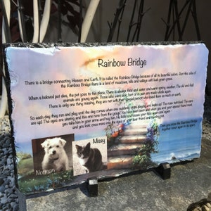 May include: A rectangular slate memorial plaque with the text "Rainbow Bridge" and a poem about pets. Includes photos of a white dog named Norman and a black and white cat named Missy. The plaque is supported by two black stands.