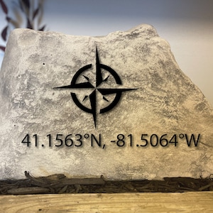 May include: A gray stone with a black compass design and the coordinates 41.1563&deg;N, -81.5064&deg;W.