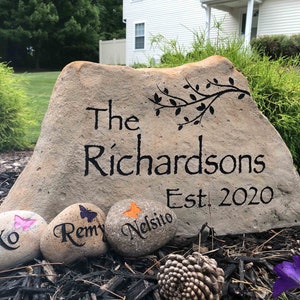 May include: A large, light brown rock with the words "The Richardsons Est. 2020" painted in black.  Three smaller rocks with painted butterflies and names are in front of the large rock.