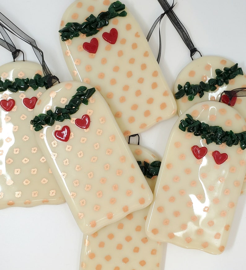 May include: Six cream-colored glass ornaments with a white polka dot pattern and red hearts. Each ornament has a green garland with a red heart at the top.