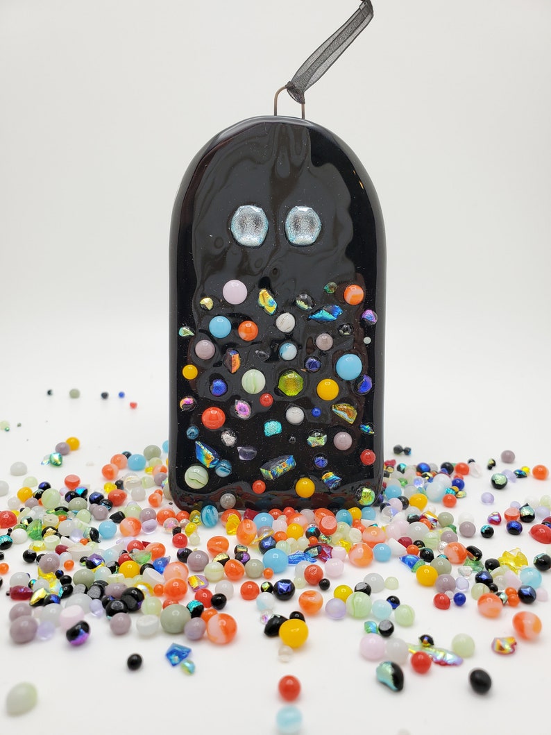 May include: Black glass ornament with a whimsical design. The ornament is covered in colorful glass beads and has two blue eyes. The ornament is hanging from a black ribbon.
