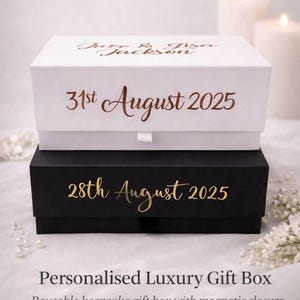 May include: Two stacked gift boxes, white on top of black, with gold text. The white box has the text "June & Lisa Jackson" and "31st August 2025." The black box reads "28th August 2025." The text at the bottom reads "Personalised Luxury Gift Box."