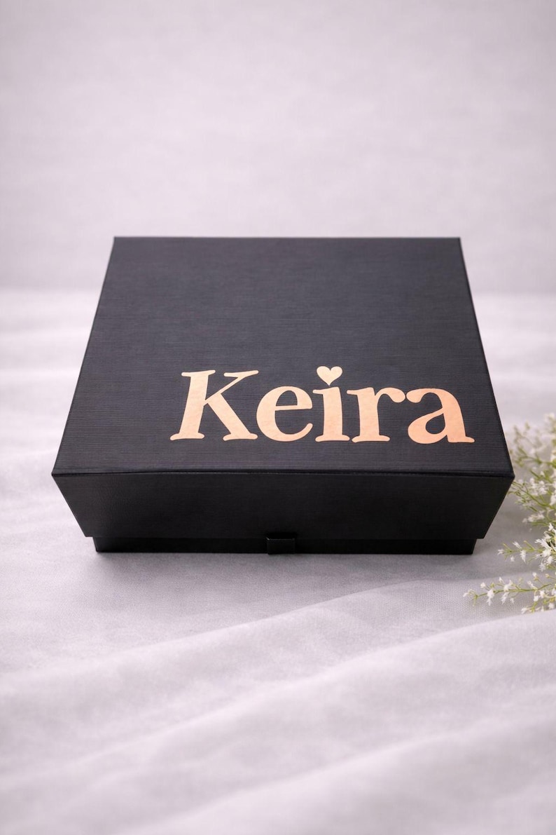 May include: A square black gift box with a textured finish. The lid features the name Keira printed in a metallic rose gold font, with a small heart icon replacing the dot above the letter i. The box has a simple, clean design.