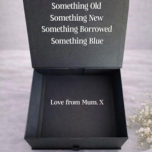 May include: A black square gift box with a hinged lid. The inside of the lid features the white text: Something Old, Something New, Something Borrowed, Something Blue. The bottom interior of the box displays the white text: Love from Mum. X.