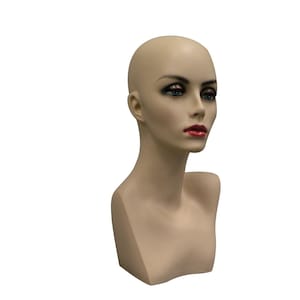 May include: A mannequin head with a bald head, painted with makeup including red lipstick and eye shadow. The mannequin has a neutral skin tone and is designed to display wigs, hats, and jewelry.