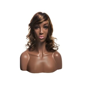 May include: A brown mannequin bust with a long, wavy brown and blonde wig. The mannequin has a neutral expression and is wearing a necklace.