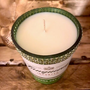 May include: A green glass candle jar with a gold glitter rim and a white candle inside. The jar is decorated with a label that says "Tanqueray" and "Imported London Dry Gin".
