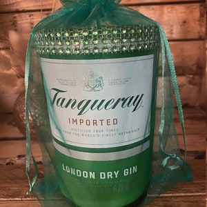May include: A green glass bottle of Tanqueray London Dry Gin, wrapped in a green tulle bag with rhinestones. The bottle label reads "Tanqueray Imported, Distilled Four Times from the World's Finest Botanicals, London Dry Gin".