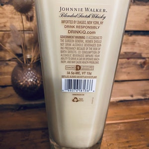 May include: A tall, clear glass filled with a creamy liquid, likely a candle. The label reads "JOHNNIE WALKER Blended Scotch Whisky." The glass is set against a wooden background. The text "DRINKIQ.com" is also visible.