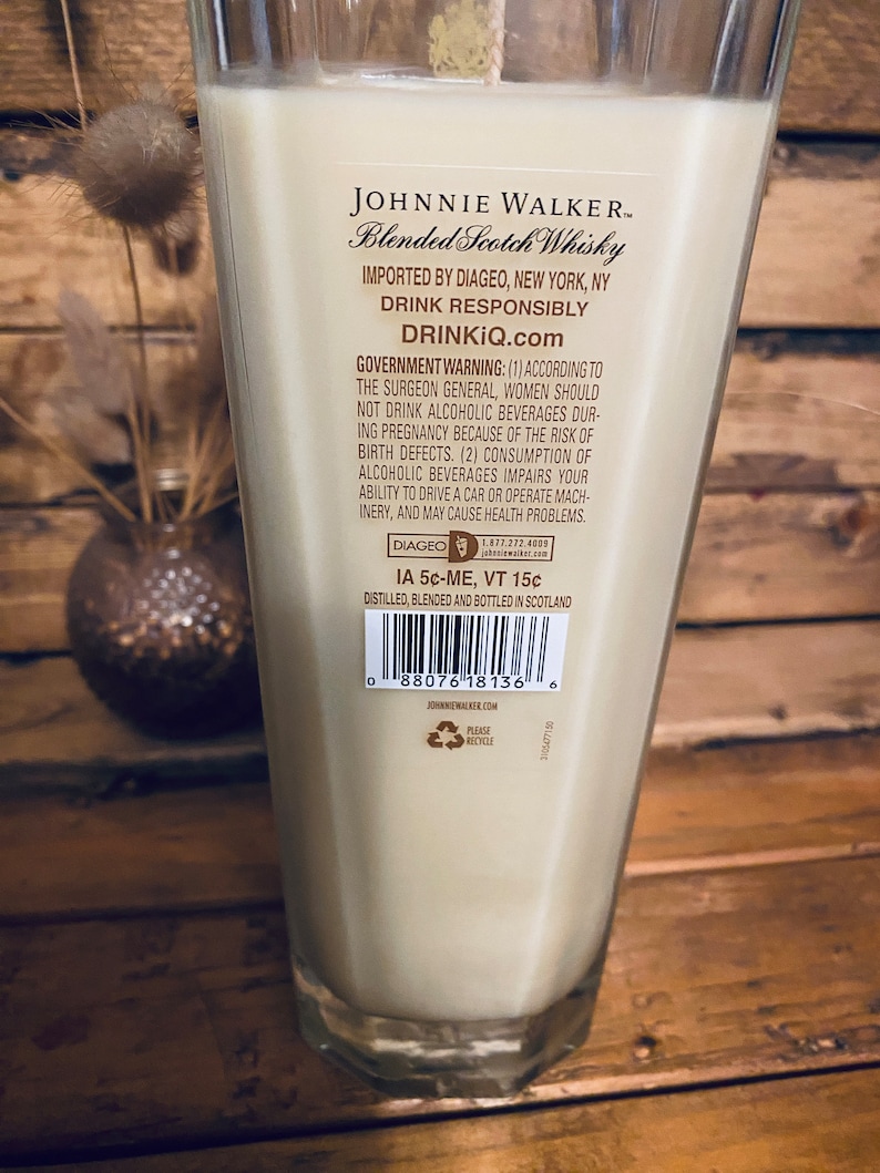 May include: A tall, clear glass filled with a creamy liquid, likely a candle. The label reads "JOHNNIE WALKER Blended Scotch Whisky." The glass is set against a wooden background. The text "DRINKIQ.com" is also visible.