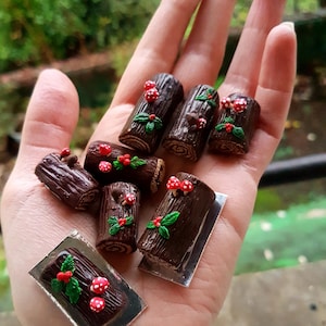 Peut inclure: Une collection de bûches de Noël miniatures en chocolat décorées de feuilles de houx vertes et de bonbons rouges et blancs. Certaines bûches sont sur un plateau argenté.
