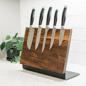 May include: A wooden magnetic knife holder with a black metal base. Five silver knives with black handles are attached to the holder.