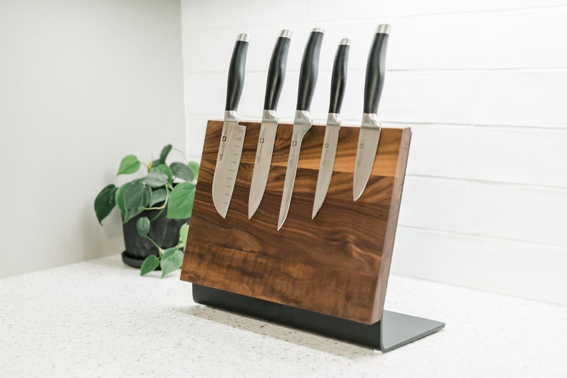 May include: A wooden magnetic knife holder with a black metal base. Five silver knives with black handles are attached to the holder.