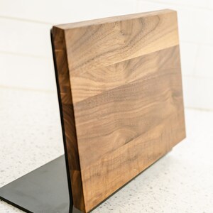 May include: A wooden magnetic knife holder with a black metal base. The holder is made of walnut wood and has a natural finish.