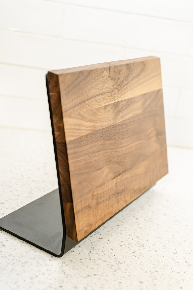 May include: A wooden magnetic knife holder with a black metal base. The holder is made of walnut wood and has a natural finish.