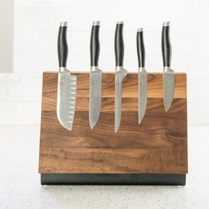 May include: A wooden magnetic knife holder with a black base, holding six silver knives with black handles.