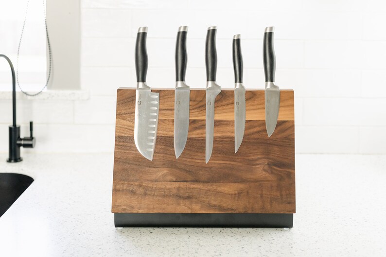 May include: A wooden magnetic knife holder with a black base, holding six silver knives with black handles.